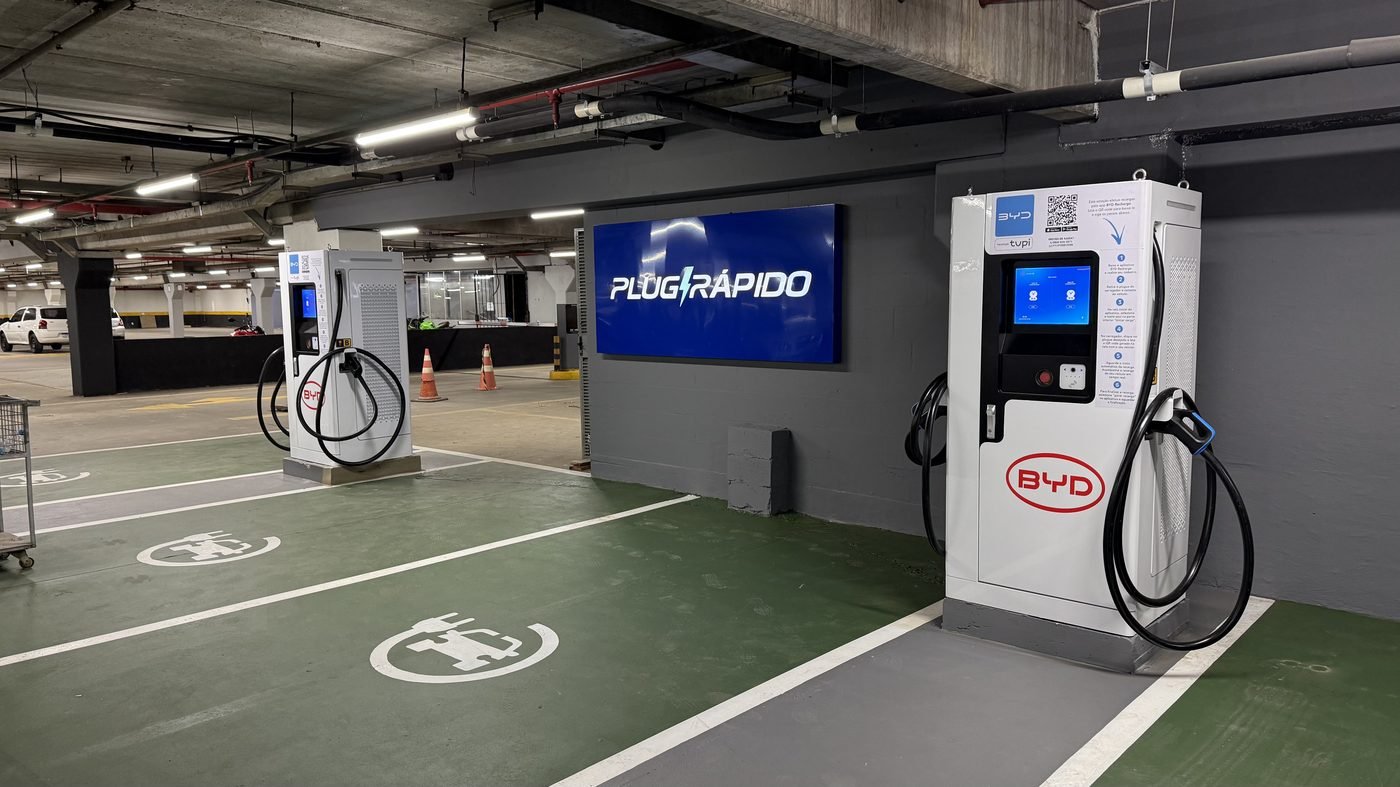Hub Plug Rápido de Recarga no estacionamento coberto do Super Andreazza, em São Leopoldo, com o letreiro da marca ao fundo e vagas sinalizadas para veículos elétricos
